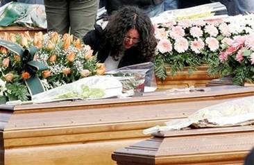 A woman reacts between coffins at the funerals for quake victims ...