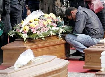 A man kneels by a coffin during the funerals for quake victims ...