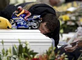 A man kisses the coffin of his son, adorned with a toy motorcycle, ...