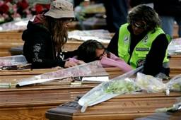 Two women react  between coffins as a field psychologist assists ...
