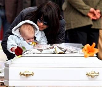 A woman with a toddler gets closer to a white coffin of a child, ...