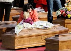 A woman and child sit between coffins at  the funerals for quake ...