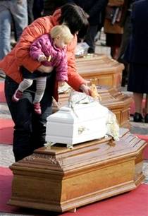 A woman with a small girl touches the white coffin of a child, ...