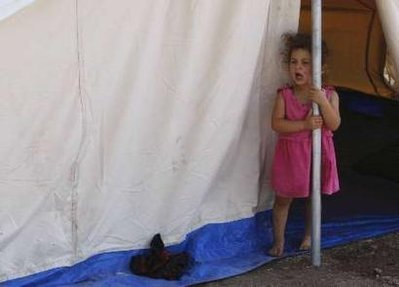 A girl stands outside a tent in a refugee camp for people displaced ...
